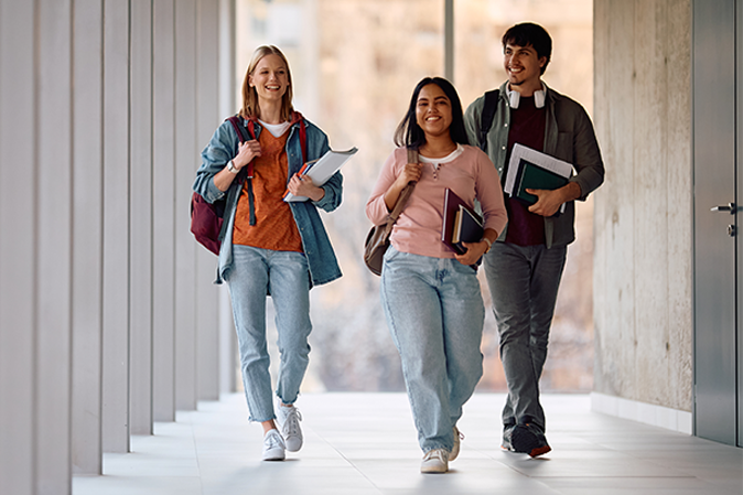 Three college students holding books and backpacks walking down a hallway