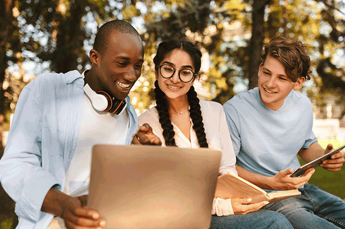 Three young students outside working together on a laptop studying