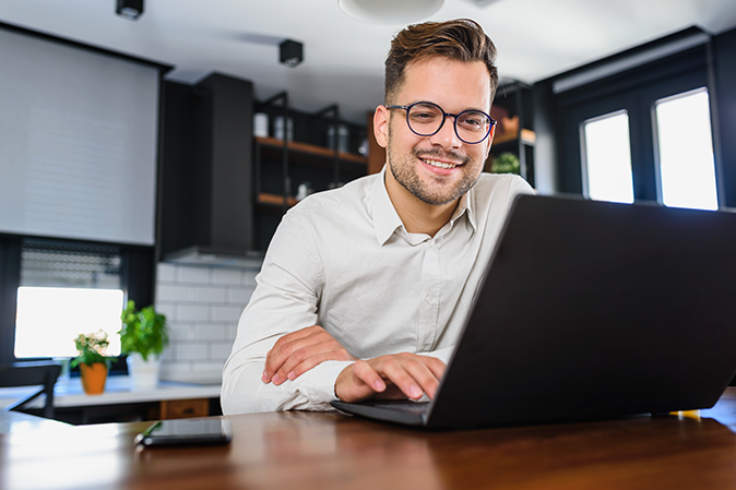 Young man smiling while typing on a laptop in an office