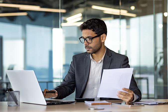 Young businessman concentrating on paperwork and laptop inside office